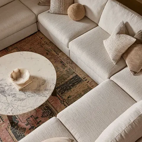 Cream sectional sofa around a round marble coffee table on a patterned rug