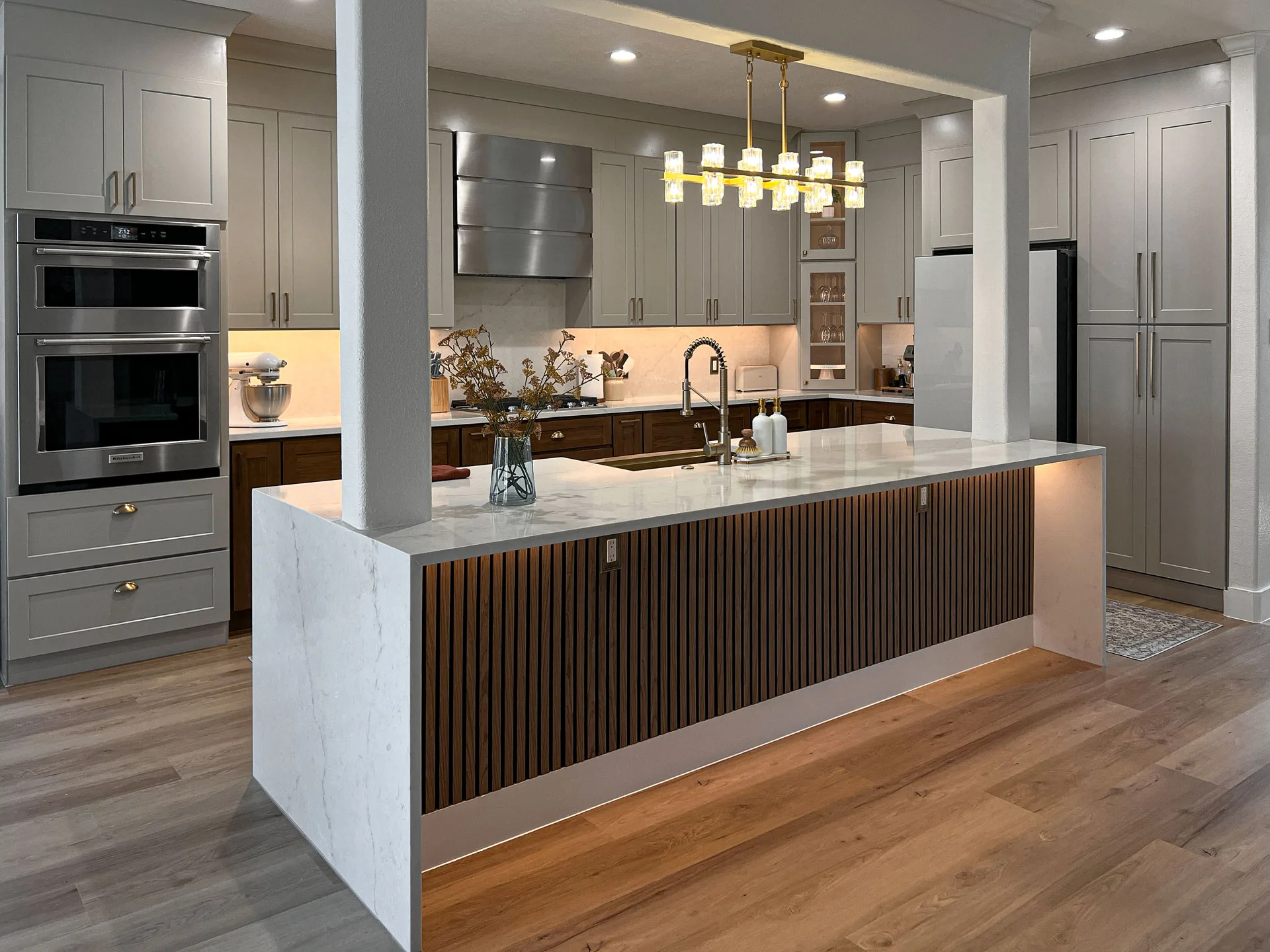 Completed Frisco kitchen with a waterfall island, walnut base cabinets, soft gray cabinetry, and wide-plank flooring