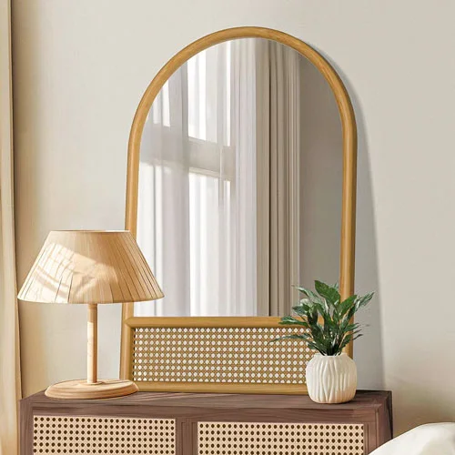 Arched wood mirror above a cane-front console with a table lamp and greenery