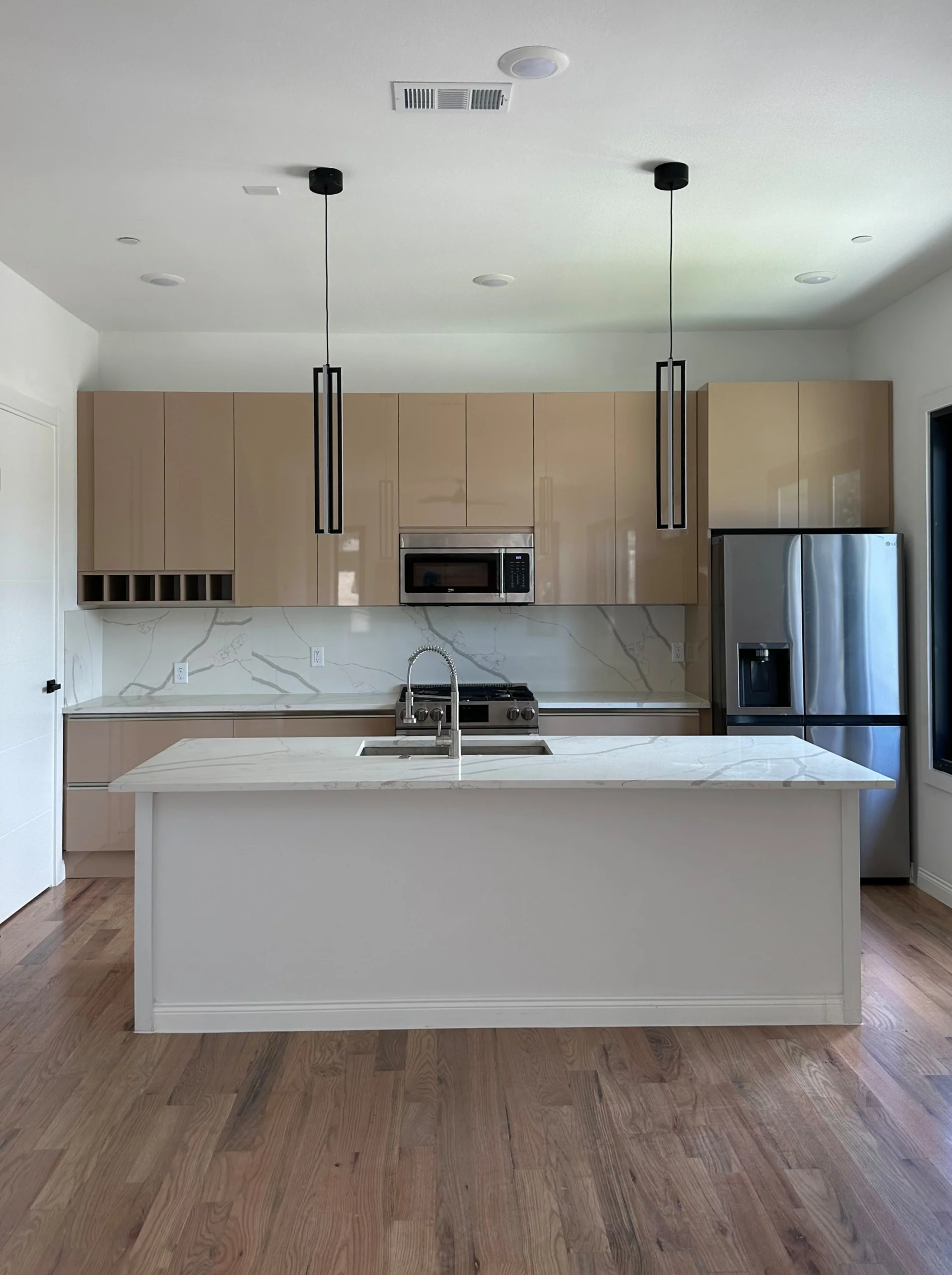 Warm neutral frameless kitchen cabinetry with a white island and pendant lights