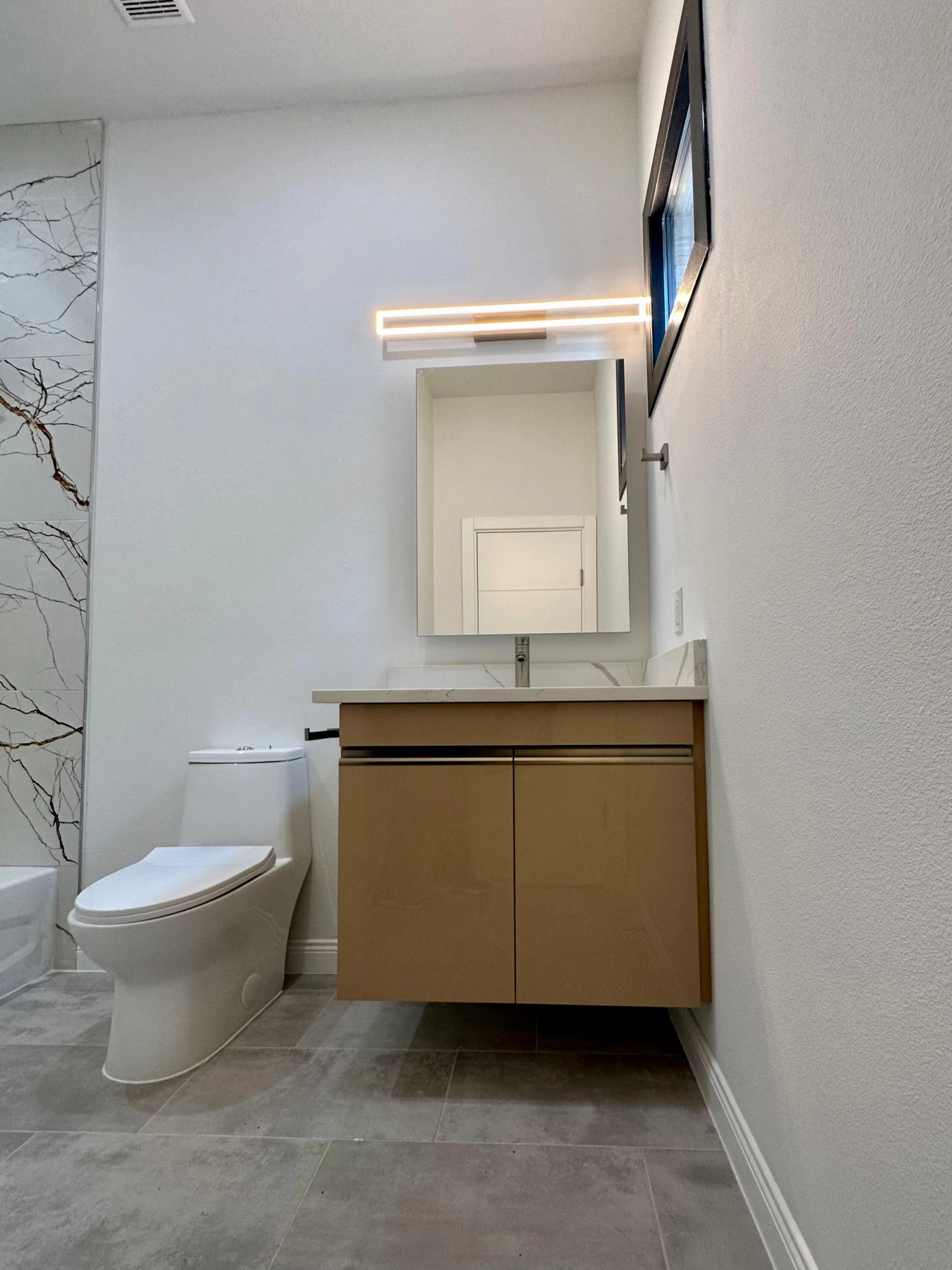Floating vanity beside a toilet and marble-look wall finish
