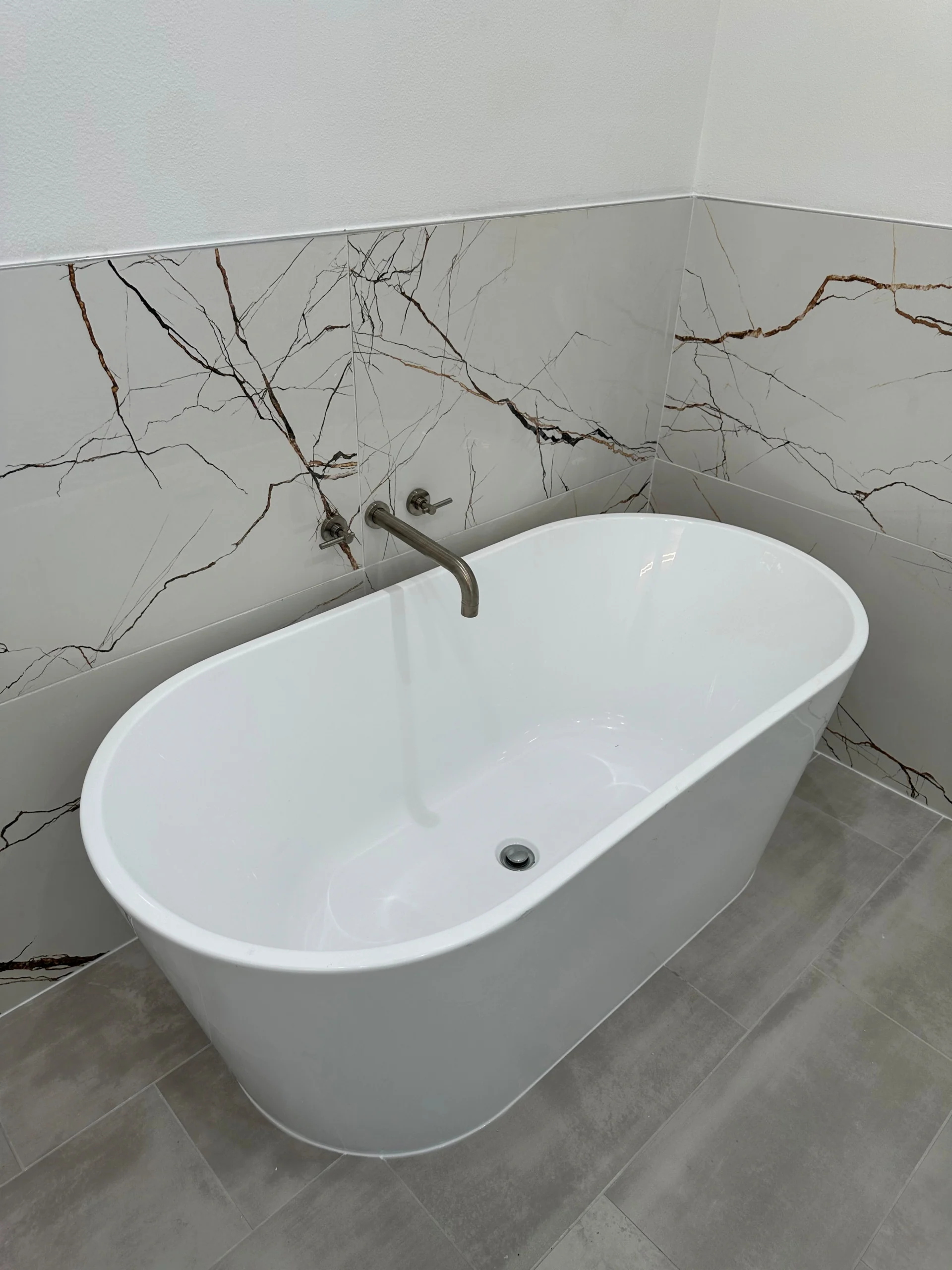 Freestanding bathtub beside a veined wall and wood-look flooring