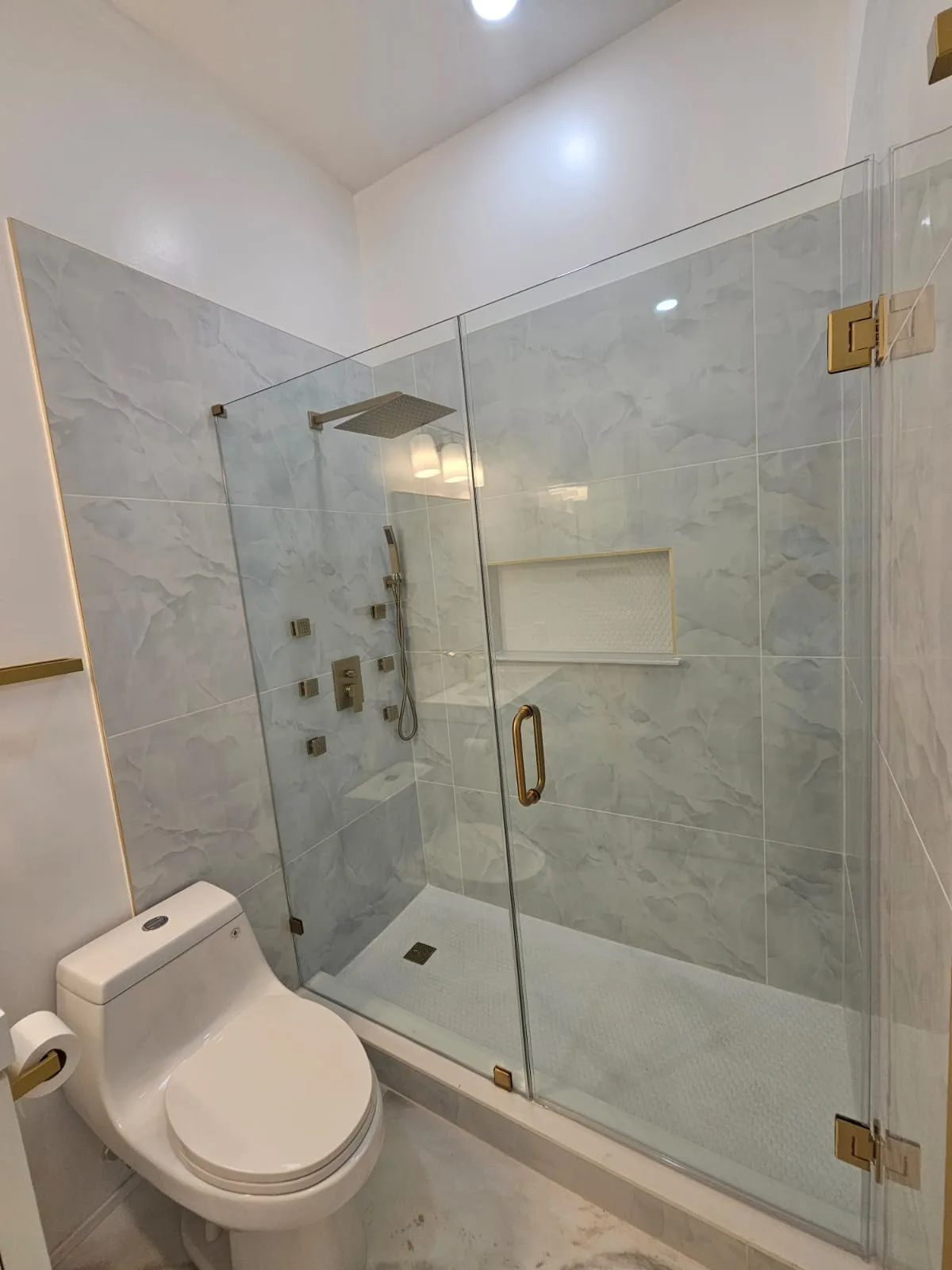 Glass shower enclosure with light veined wall tile, a recessed niche and warm metal hardware