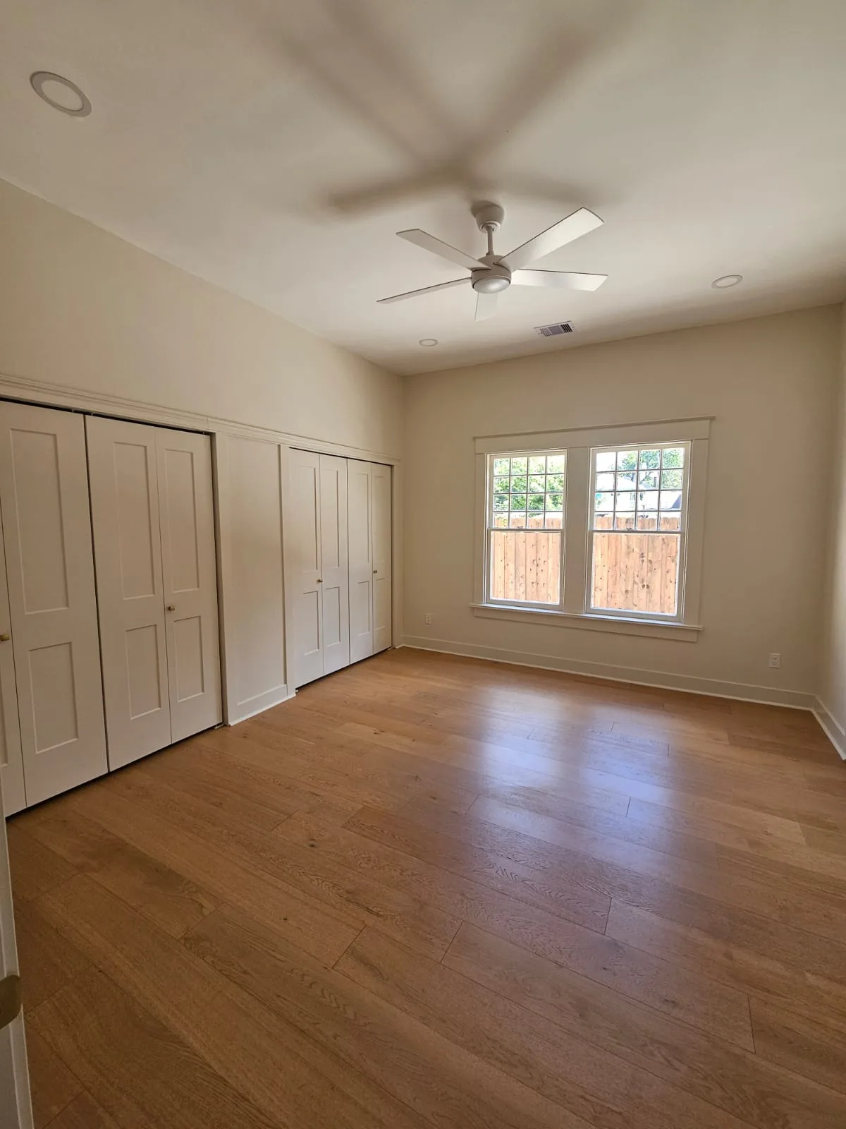Bedroom with warm plank flooring, light painted walls and white closet doors