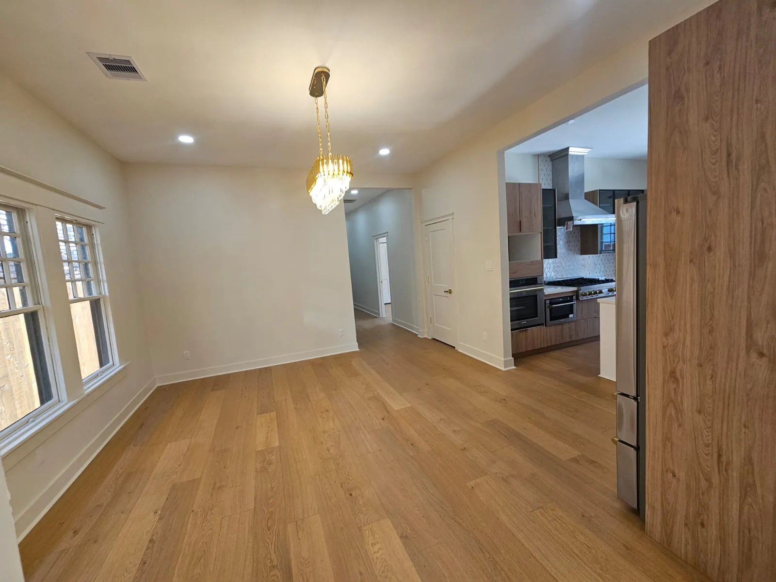 Dining area with warm plank flooring, light painted walls and a view into the kitchen