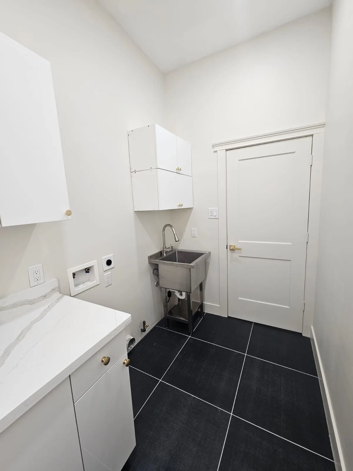 Laundry room with white cabinetry, a veined counter, a utility sink and dark floor tile