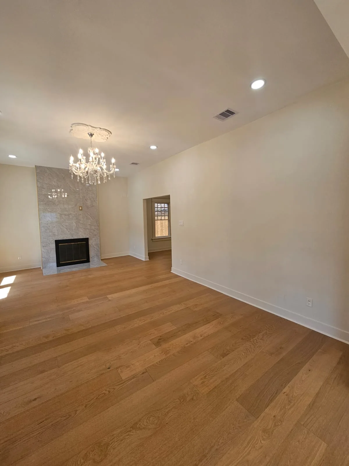 Renovated living room with warm plank flooring, light walls and a veined fireplace surround