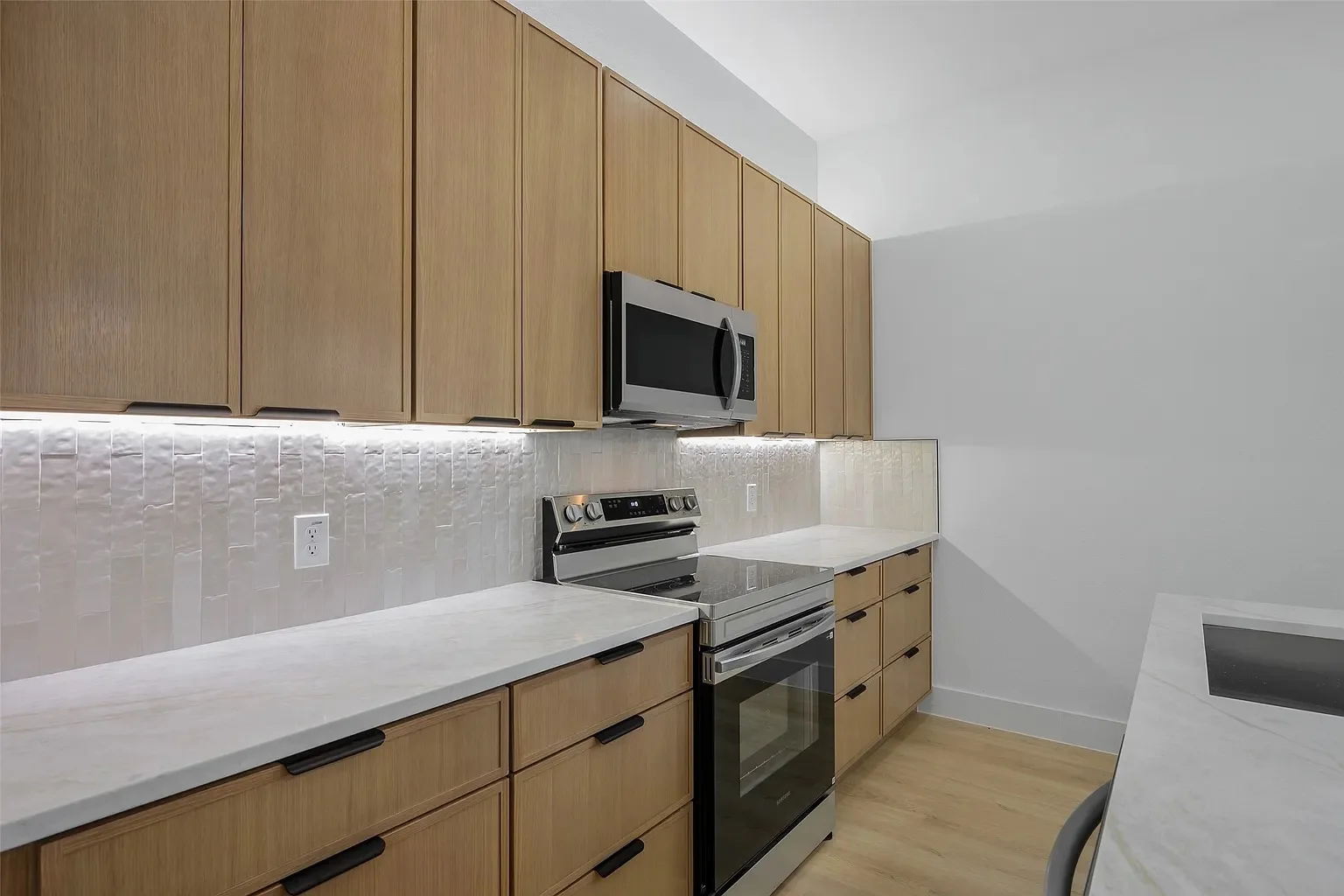 Wood-toned kitchen cabinets with black pulls, light countertops and a textured tile backsplash