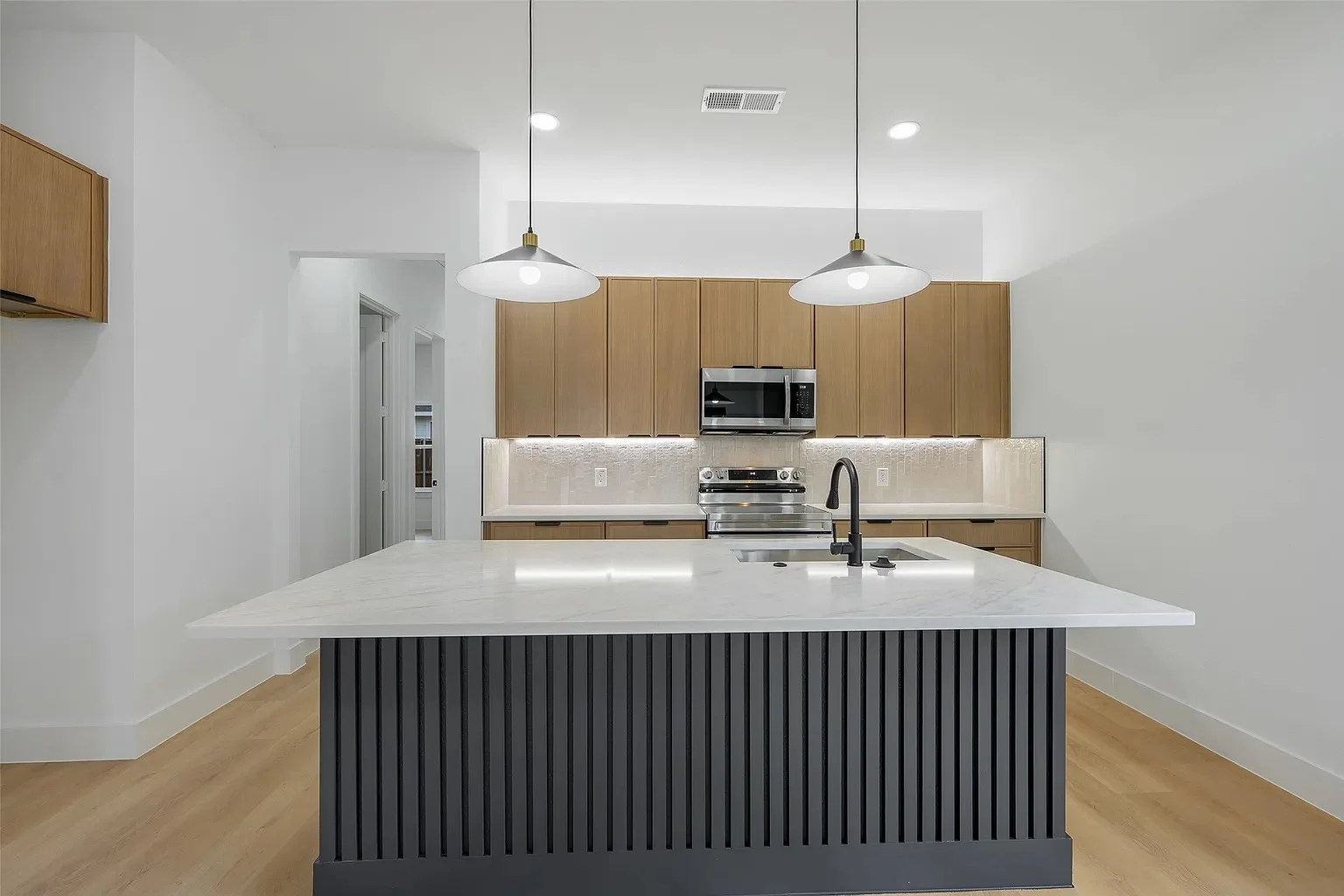 Completed kitchen remodel with wood-toned cabinetry, a dark fluted island and light veined countertops